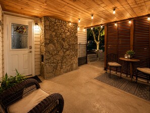 A covered patio with a stone wall, a wooden ceiling, and a seating area with a table and chairs.