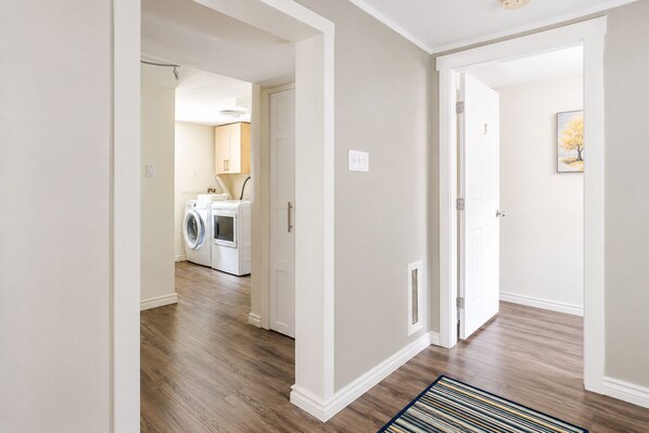 A hallway with a laundry area, wooden flooring, and a door leading to another room.