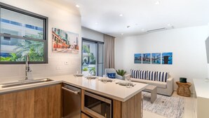 A modern kitchen with a built-in dishwasher, a dining area with a sofa and a coffee table, and a living room with a sofa and a TV.