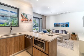 A modern kitchen with a built-in dishwasher, a dining area with a sofa and a coffee table, and a living room with a sofa and a TV.