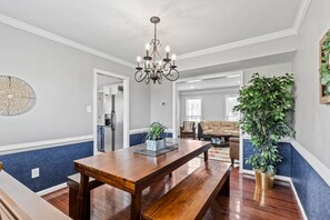 Een ruime woonruimte met een houten eettafel, een kroonluchter en een grote potplant.