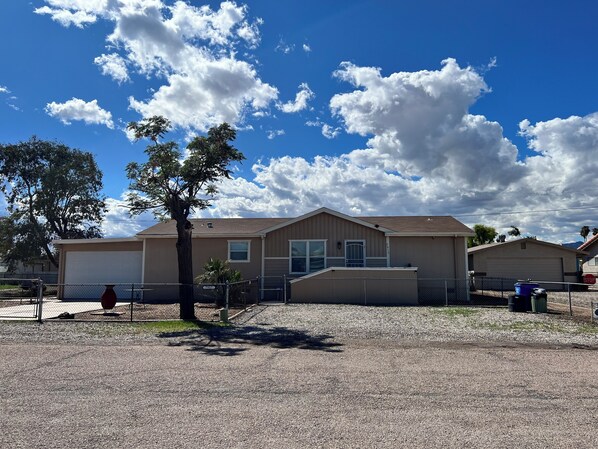 A two-story building with a garage, a fenced driveway, and a tree in front.