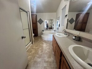 A bathroom with two sinks, a bathtub, and a shower. There is a mirror above the sink and a door on the left.