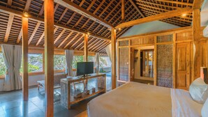 A spacious room with a large bed, wooden ceiling beams, a television on a wooden table, and a view of greenery outside. - Villa Teman-Luxury 4BR Villa in Seminyak (Seminyak)