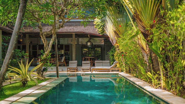A pool area with lounge chairs and a dining area, surrounded by lush greenery. - Villa Teman-Luxury 4BR Villa in Seminyak (Seminyak)
