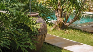 A garden with a variety of tropical plants, a decorative stone planter, and a swimming pool. - Villa Teman-Luxury 4BR Villa in Seminyak (Seminyak)