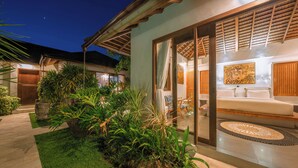 A modern house with a glass door leading to a living area with a sofa and a painting. There is a garden with various plants and a pathway. - Villa Teman-Luxury 4BR Villa in Seminyak (Seminyak)