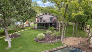 A two-story house with a covered porch, surrounded by a well-maintained lawn and a small pond.