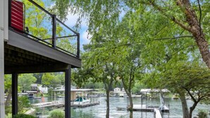 A covered outdoor area with a pathway leading to a dock by a lake, surrounded by greenery and trees.