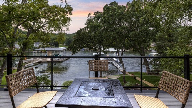 A balcony with wicker chairs and a table, overlooking a body of water with a dock and boats.