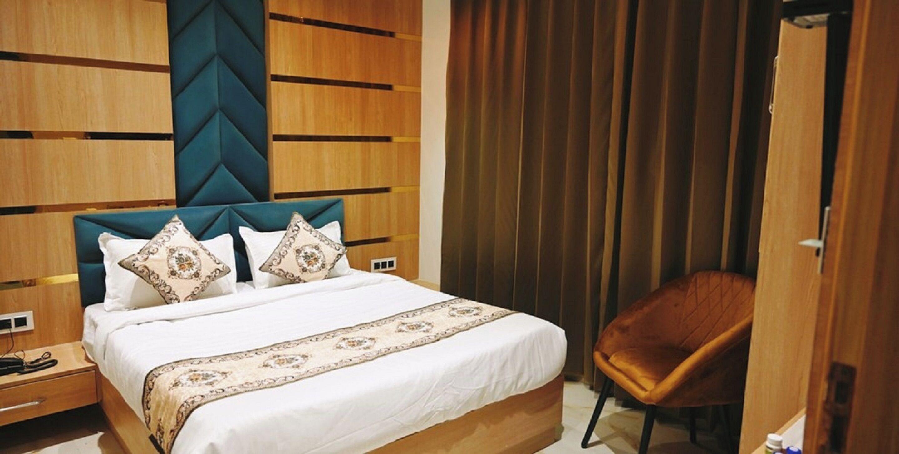 A hotel room with a bed, a wooden headboard, a chair, and a wardrobe.