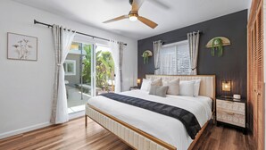 Ein Schlafzimmer mit Bett, Deckenventilator, Nachttischlampen und Blick ins Freie.