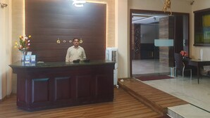 A reception desk with a man standing behind it, a modern chandelier, and a wooden reception desk. - Hotel Shrinath Palace (Jhansi)