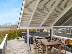 Una terraza cubierta al aire libre con mesa y sillas, una parrilla y vistas del paisaje circundante.