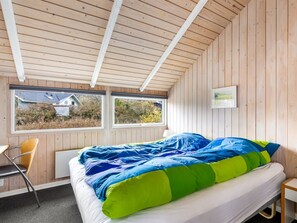 Un dormitorio con una cama, dos ventanas, una silla y un cuadro en la pared.