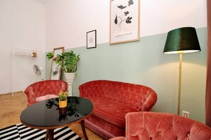 A living room with a red velvet sofa, a black round table, a green floor lamp, and a framed floral artwork on the wall.