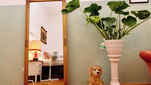 A room with a wooden floor, a white bedside table with a lamp, a mirror, a potted plant, and a red chair. - Romantic Urban Living (Vienna)