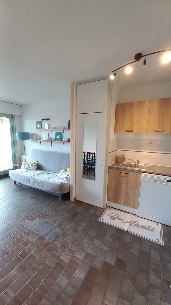 Un apartamento moderno con sala de estar que incluye un sofá, una mesa de comedor con sillas, una cocina con armarios de madera y una ventana pequeña.