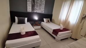 A hotel room with two beds, a nightstand, a lamp, and a window with curtains. - Coron Town Travellers Inn (Coron)