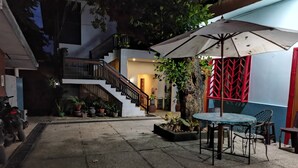 A courtyard with a staircase, potted plants, a table with chairs, and a red decorative wall. - Coron Town Travellers Inn (Coron)