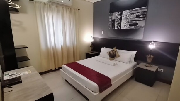 A modern hotel room with a large bed, a desk, and a nightstand. - Coron Town Travellers Inn (Coron)