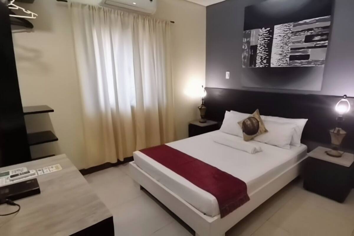 A modern hotel room with a large bed, a desk, and a nightstand.