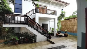 A modern two-story house with a staircase, potted plants, and a bamboo fence. - Coron Town Travellers Inn (Coron)
