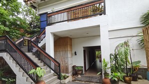 A two-story building with a staircase leading to a balcony. There are potted plants around the entrance and along the pathway. - Coron Town Travellers Inn (Coron)