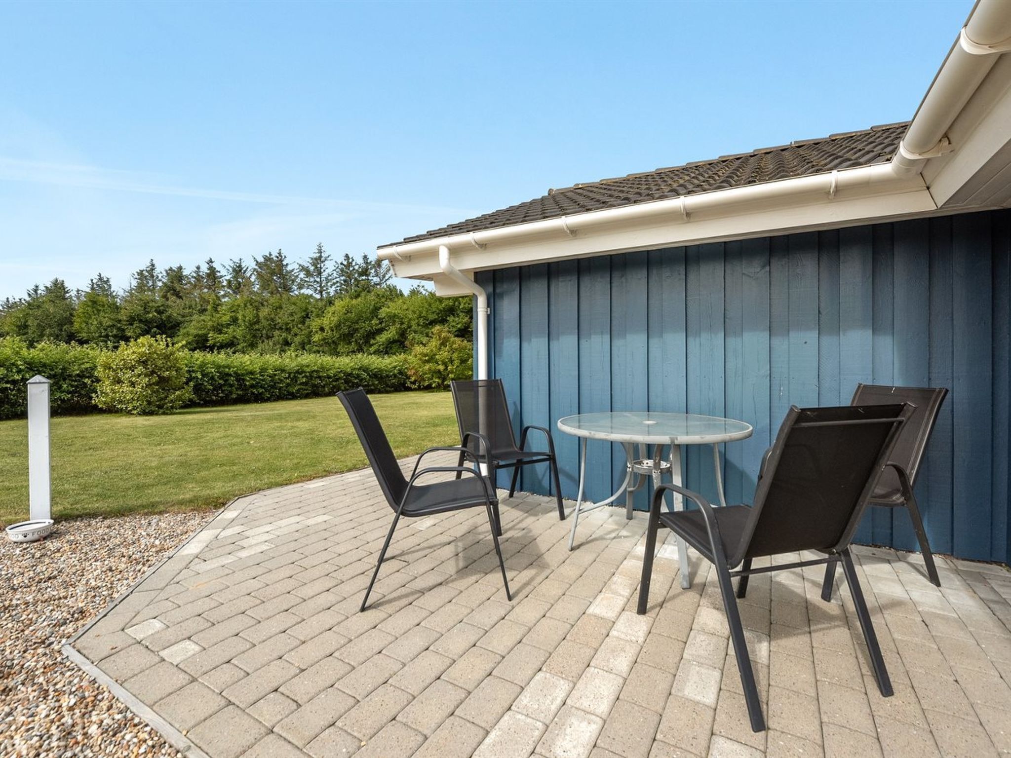 An outdoor patio with a table and chairs, a blue wall, and a grassy area with trees.