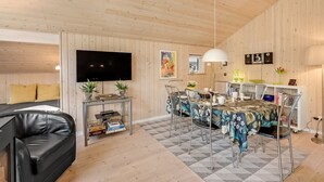 Een moderne woonkamer met een flatscreen televisie, een zwarte leren bank, een eettafel met stoelen en houten wanden.