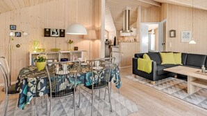 Een gezellig, goed verlicht houten interieur met een eethoek, een bank en een keuken in de achtergrond.