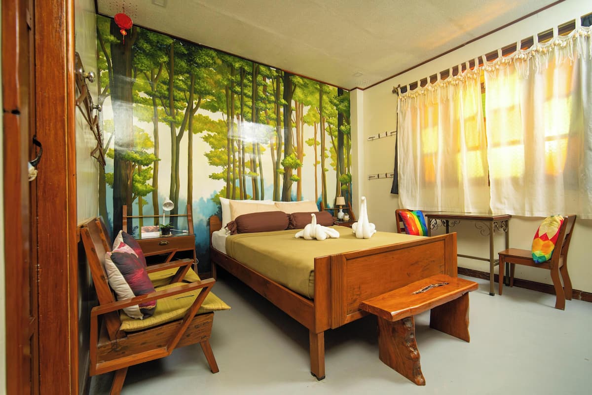 A bedroom with a large bed, a wooden chair, a small table, and a window with curtains.