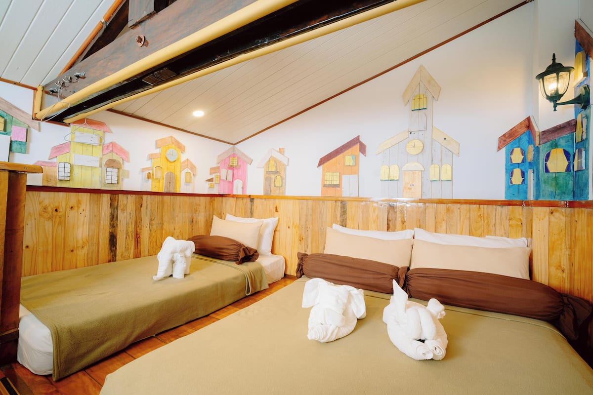 A room with two beds, wooden walls, and a mural of colorful houses.