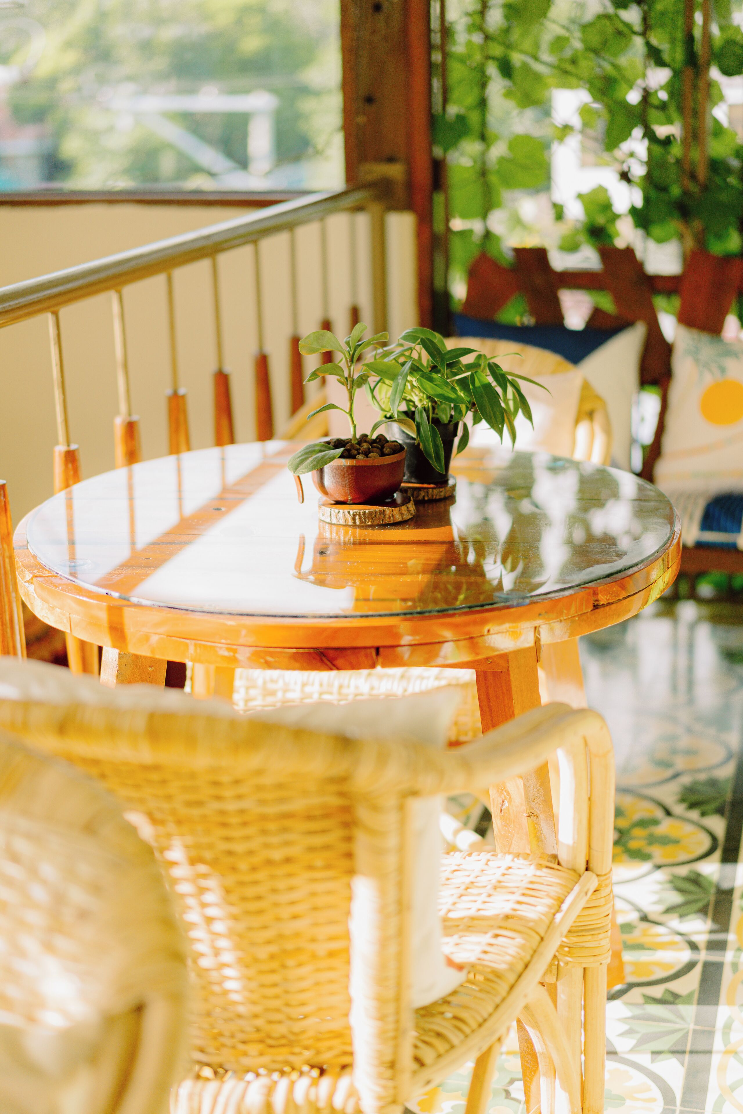 A round glass table with a potted plant, wicker chairs, and a tiled floor with a floral pattern.
