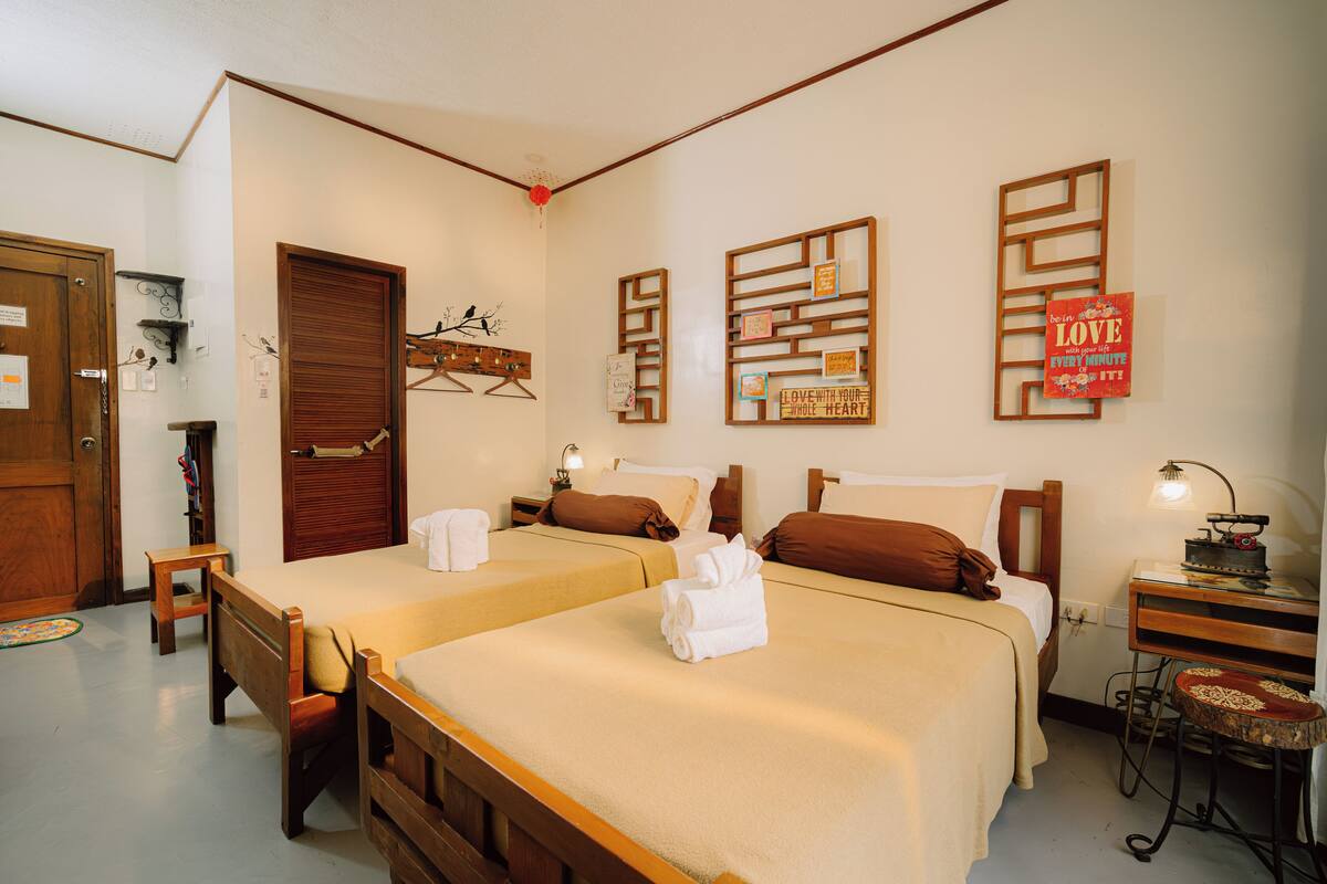 A hotel room with two beds, wooden headboards, and a desk with a lamp.