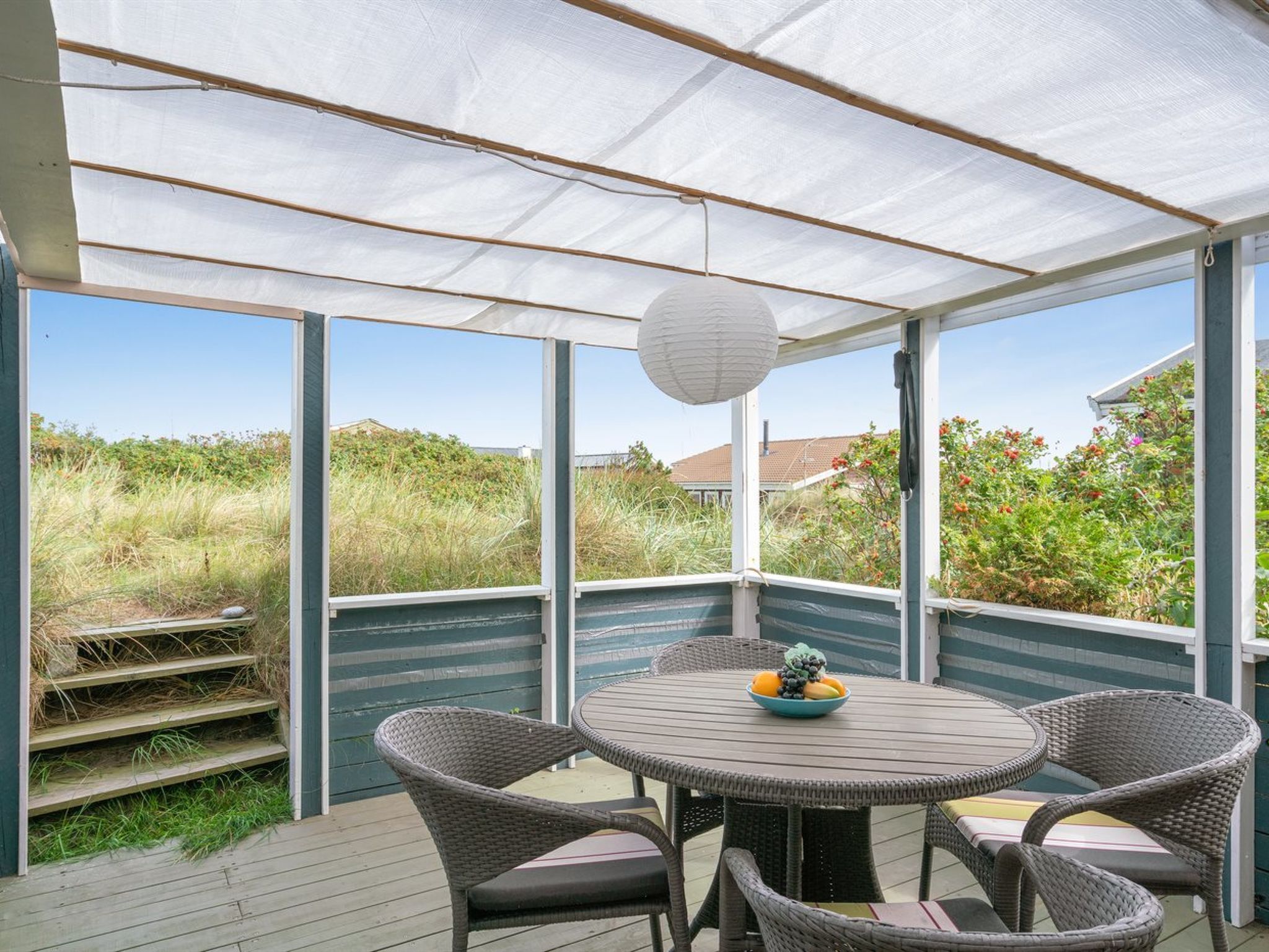 A covered patio area with wicker furniture and a table with a fruit bowl.