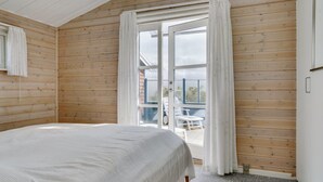A bedroom with a bed, wooden walls, a window with curtains, and a view of the outside. - "Stener" - 250m from the sea by Interhome (Thisted)