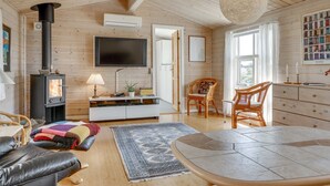 A cozy cabin interior with a wood stove, a flat-screen TV, a dining table, and a large window. - "Stener" - 250m from the sea by Interhome (Thisted)