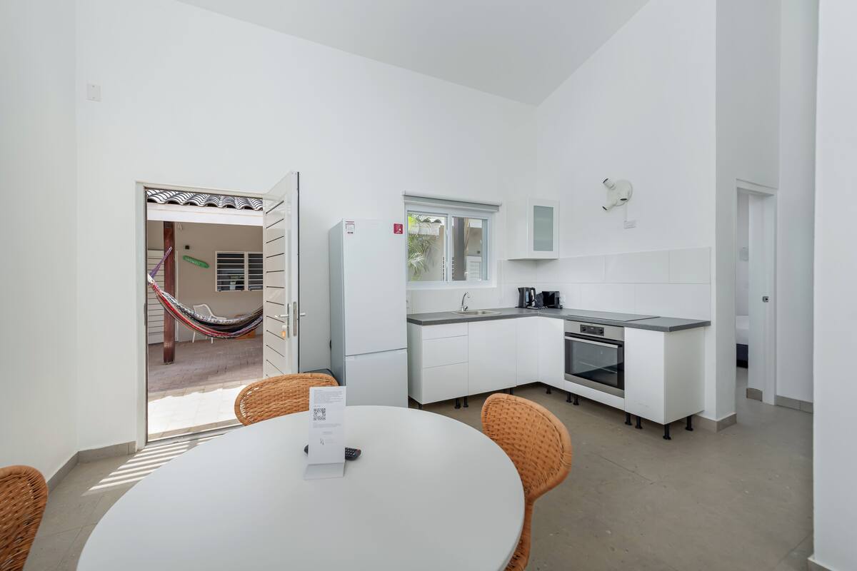 A modern kitchen with white cabinetry, a built-in oven, and a dining area with wicker chairs and a round table.