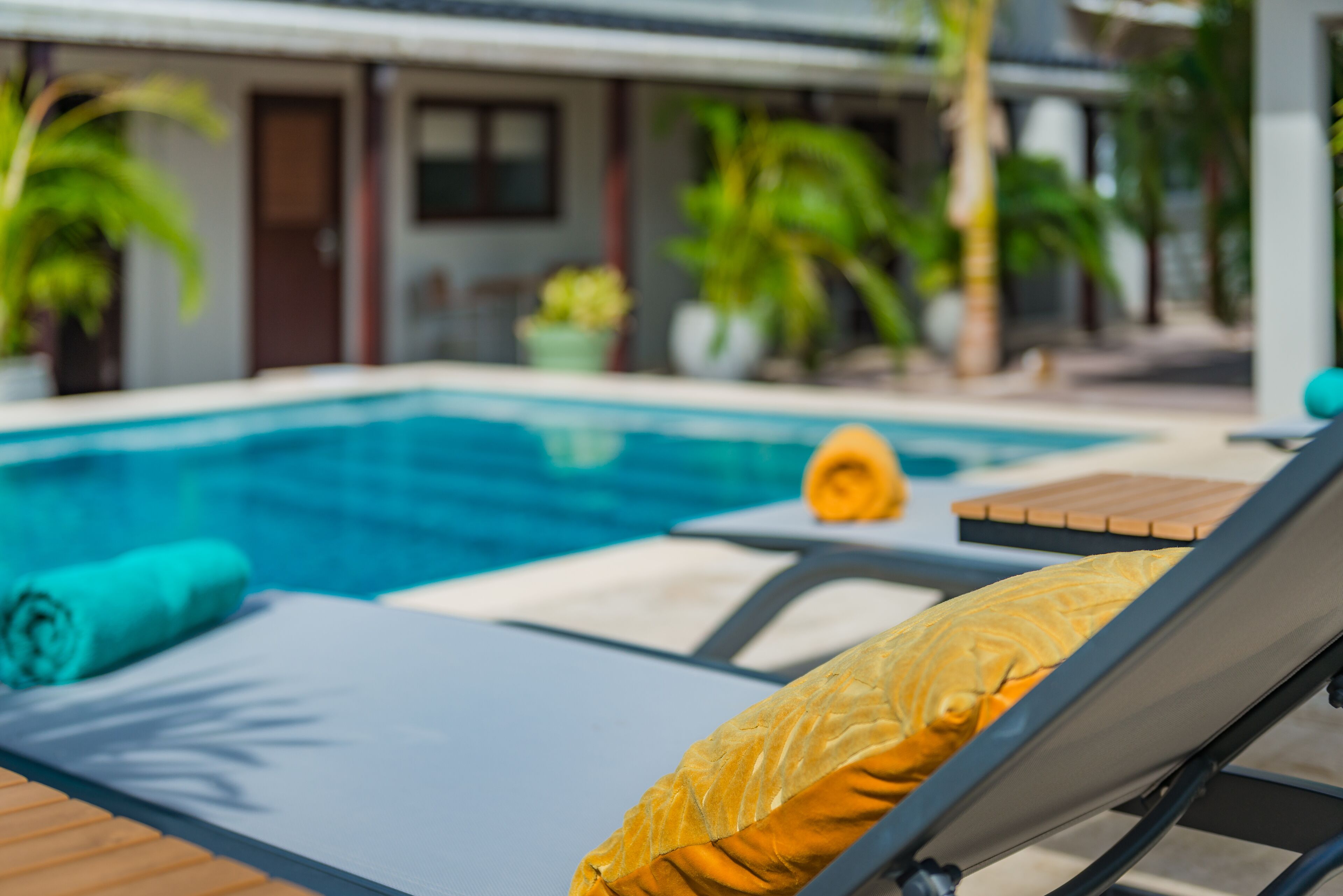 Un área junto a la piscina con una silla de descanso, una toalla enrollada y un almohadón amarillo.