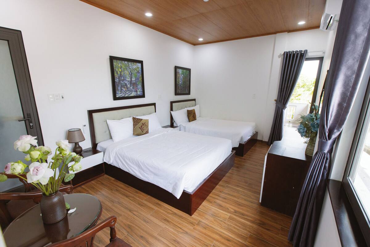 Habitación de hotel con dos camas, piso de madera, un escritorio con silla y una ventana con cortinas.