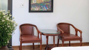 Una habitación con dos sillas de madera y una pequeña mesa redonda, un cuadro en la pared y una planta en maceta.