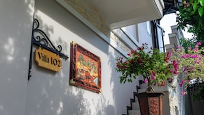 Entrada de un edificio con un letrero de madera que dice “Villa 102”, un mural decorativo y una escalera con una jardinera.