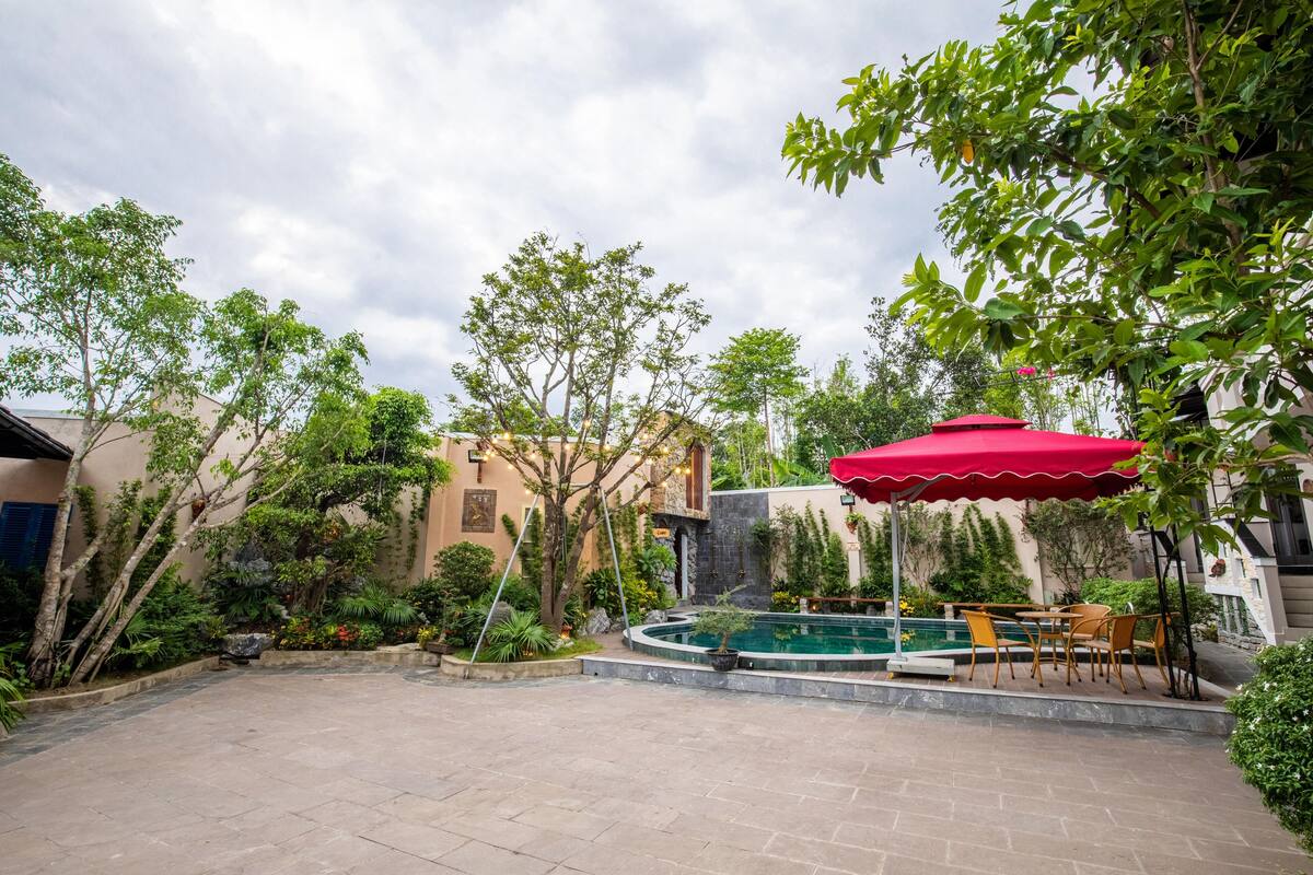 Un área de patio al aire libre con piscina, sombrilla roja y mobiliario exterior.