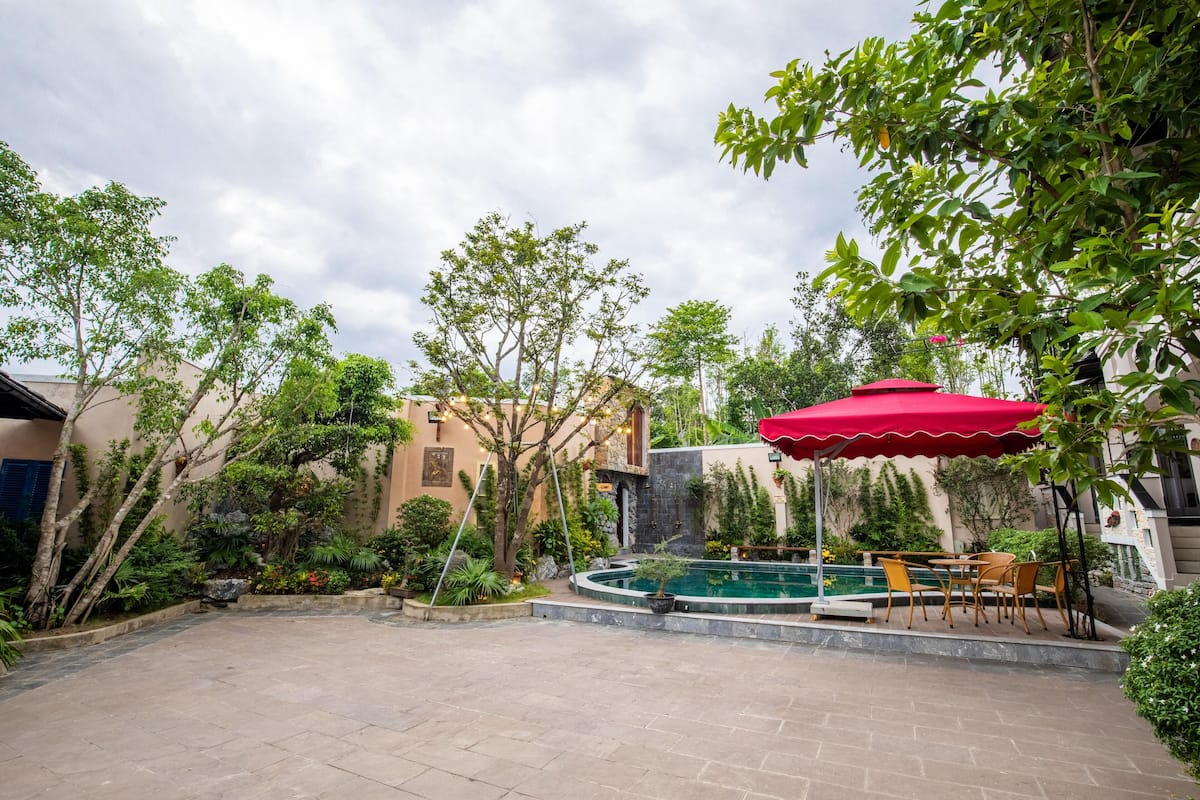An outdoor patio area with a pool, red umbrella, and outdoor furniture.