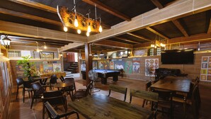 Interior de restaurante con mesas y sillas de madera, una mesa de billar y un televisor montado en la pared.