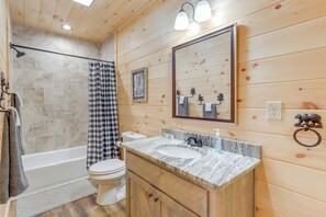 A bathroom with a wooden interior, a bathtub, a toilet, and a vanity with a sink and mirror. - Cabin Near Blue Ridge w/ Fire Pit & Large Deck (Mineral Bluff)