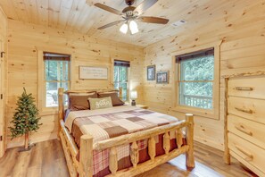 A log cabin bedroom with a wooden bed, a ceiling fan, and a Christmas tree. - Cabin Near Blue Ridge w/ Fire Pit & Large Deck (Mineral Bluff)