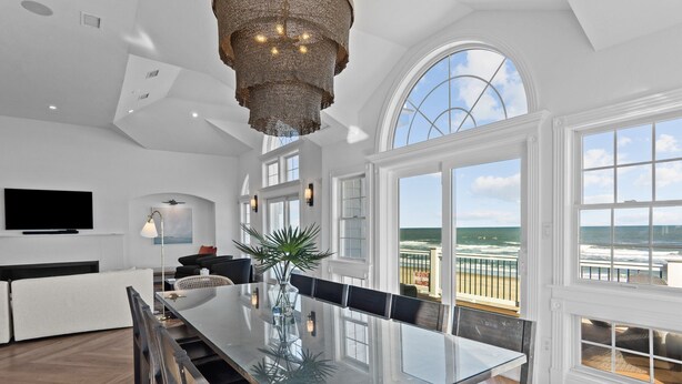 A spacious dining area with a glass table, white walls, and large windows overlooking the ocean. - 2876 - The Blue Martini - Oceanfront Luxury Retreat w/ Pool & Sauna (Duck)