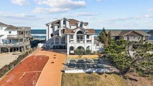 A large, multi-story house with a balcony overlooking the ocean, a driveway, and a well-maintained lawn. - 2876 - The Blue Martini - Oceanfront Luxury Retreat w/ Pool & Sauna (Duck)